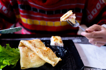 Close up shot of a ham and cheese crepe garnished with a lettuce leaf. The fork has a bite ready to eat.