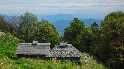 Fototapeta na wymiar An abandoned wooden sheepfold in a beautiful pasture, surrounded by a beech forest. Autumn season. The far away crests of Cozia Mountains can be seen along the horizon. Buila, Carpathia, Romania.