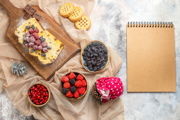 top view raisin cake on cutting board bowl with pomegranate raspberry candies and raisins biscuits on beige tablecloth a notebook on marble ground