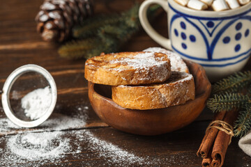 French toast with powdered sugar and cinnamon, a Cup of cocoa with marshmallows, fir branches on a dark wooden table top