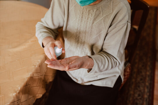 Close up of a senior woman pouring an antibacterial hand sanitizer into her hand while sitting at a table in the house. Hygiene during the COVID-19 coronavirus pandemic - Powered by Adobe