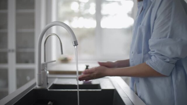 Young woman standing at sink washing her hands carefully in kitchen