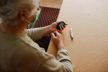 Close-up of a senior woman who measures blood sugar with a device in her house. Health prevention during the COVID-19 coronavirus pandemic