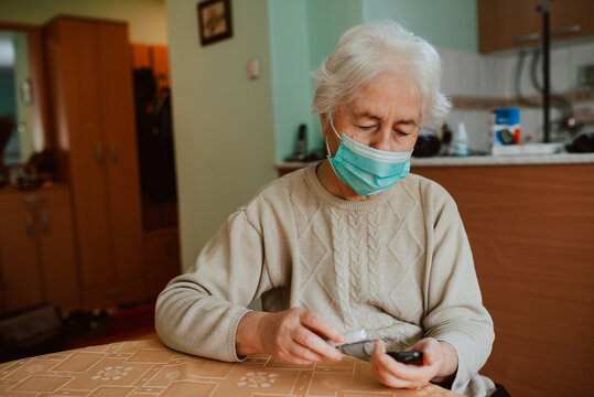 A Caucasian senior woman with a face mask that controls her health with a device for measuring blood sugar in her house. Health prevention during the COVID-19 coronavirus pandemic