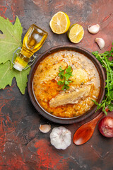 top view chicken soup garlic red onion wooden spoon oil parsley lemon slices and plane tree leaves on dark red background
