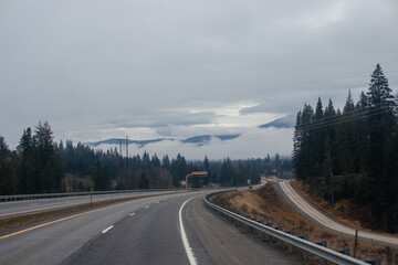 Highway with road signs on the sides among high mountains in the clouds in winter, along which trucks and cars travel. Idaho, USA, 12-5-2020