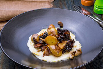 Fried potatoes with mushrooms on dark plate