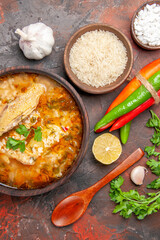 top close view chicken and rice soup in a bowl wooden spoon bowls with sea salt and rice garlic parsley leaves hot peppers slice of lemon on dark red background
