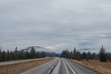 Highway with road signs on the sides among high mountains in the clouds in winter, along which trucks and cars travel. Idaho, USA, 12-5-2020