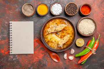 top view bowl of chicken soup bowls with different spices bowl of rice hot peppers a notebook on dark red background