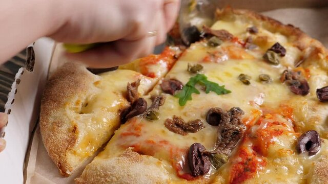 Cut with knife Fresh baked italian pizza Alla Putanesca in cardboard box on wooden table