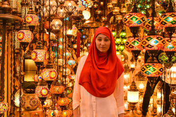 Young pretty tourist Muslim woman with red scarf looking on Traditional Turkish lamps in souvenir shop. Woman in hijab shopping in the Grand Bazar. Shopping tour.