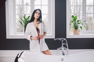Woman In Bathroom. beautiful girl on bathtub in underwear. Sex woman taking relaxing bath in jacuzzi. Beautiful sexy lady elegant white shirt in bathroom. Fashion portrait model on bath indoors