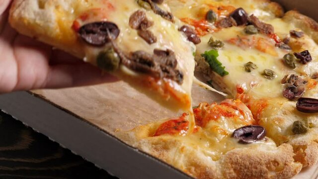 Taking one piece of Fresh baked italian pizza Alla Putanesca in cardboard box on wooden table