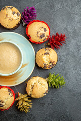 Fototapeta na wymiar Vertical view of delicious coffee around small cupcakes and new year decorations on dark background