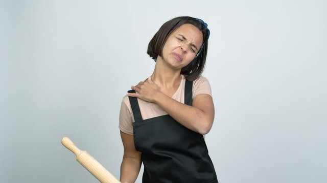Young latin woman holding a rolling pin with shoulder pain over isolated background