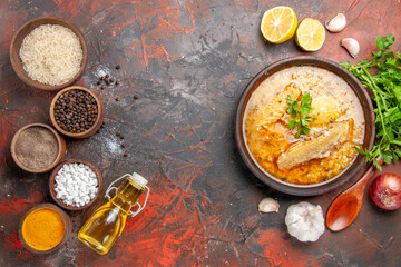 top view chicken soup garlic red onion wooden spoon oil parsley lemon slices and bowls with rice black pepper sea salt turmeric on dark red background with copy space