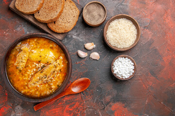 top view chicken soup bowls with pepper rice sea salt garlic spoon bread slices on cutting board on dark red background with copy space