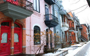 Beautiful houses of old historical Montreal neighborhood Plateau Mont Royal in winter season, bright painted doors and walls of expensive homes in gentrification-damaged area.