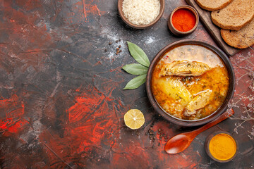 top view chicken soup bowl with rice slice of lemon bread slices on cutting board red pepper powder turmeric wood spoon on dark red background with copy space