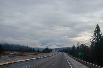 Highway with road signs on the sides among high mountains in the clouds in winter, along which trucks and cars travel. Idaho, USA, 12-5-2020