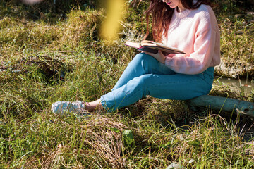 Smiling woman reading a book sitting in a tree trunk in a park. Woman in nature enjoying herself carefree.