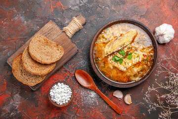 top view chicken and rice soup in a bowl wooden spoon bowl with sea salt garlic slices of bread on chopping board on dark red background
