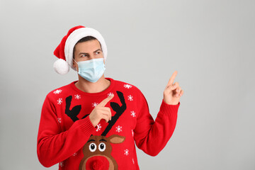 Man wearing Santa hat and medical mask on grey background