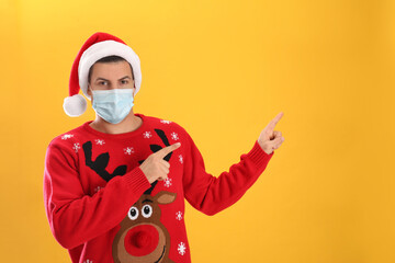 Fototapeta na wymiar Man wearing Santa hat and medical mask on yellow background, space for text