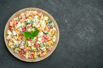 top close view of bowl of vegetable salad on the left side with green on it on dark green background