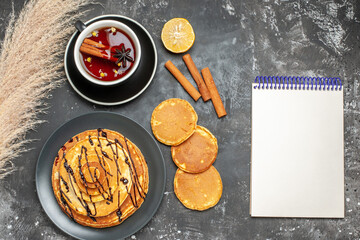 Horizontal view of delicious pancakes with chocolate and a cup of cinammon tea next to notebook on gray background