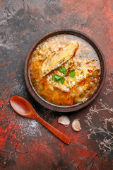 top view homemade chicken and rice soup in a bowl wooden spoon garlic on dark red background with copy space