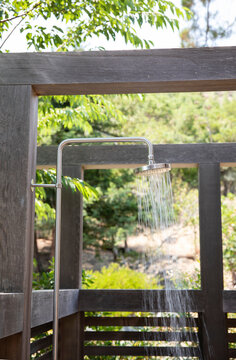 Outdoor shower  with modern wood beams surrounded by green trees.