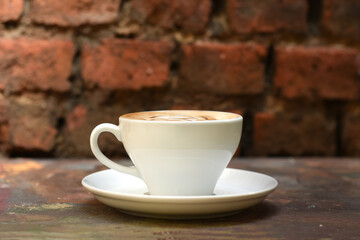 Flavored coffee in white cup on the wooden table. Background with red brick wall. 
