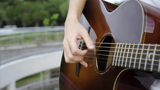 Close up shot of man playing brown guitar and plucking the strings with scenic background