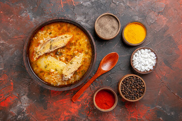 top view bowl of chicken soup bowls with different spices wooden spoon on dark red background