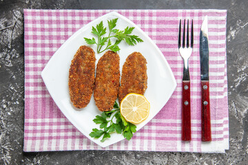 top view cutlets lemon slice parsley on white platefork and knife kitchen towel on grey background