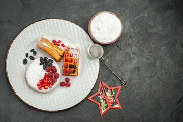 top view tart and waffles with pomegranate raisin raspberry a bowl of powdered sugar and a sieve on dark background with copy space