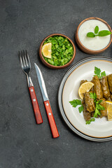 top view stuffed grape leaves on white plate bowl of parsley and natural yogurt knife and fork on dark background
