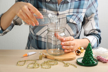 Woman making beautiful snow globe at wooden table, closeup