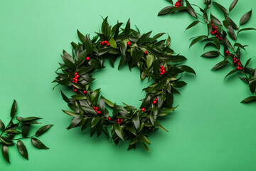 Fototapeta na wymiar Beautiful handmade mistletoe wreath on green background, flat lay. Traditional Christmas decor