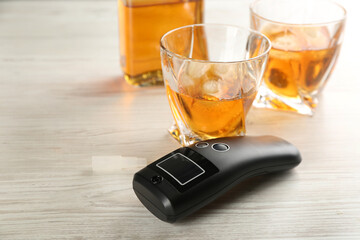 Modern breathalyzer and alcohol on white wooden table
