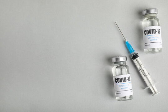 Vials with coronavirus vaccine and syringe on light background, flat lay. Space for text