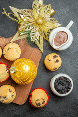 Above view of tea break with delicious small cupcakes black raisins and chocolate in a white pot on black background