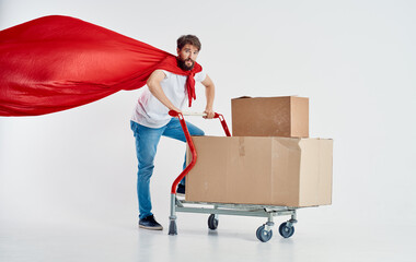 courier with cardboard boxes in cargo trolley and red superhero cloak