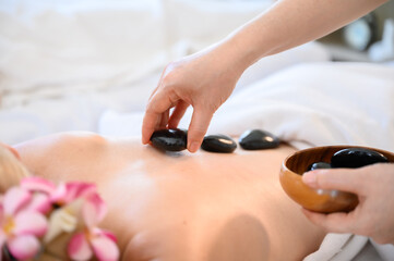 Obraz na płótnie Canvas Spa hot stone thai massage beauty treatment.Young woman getting black hot stone on back her in spa salon