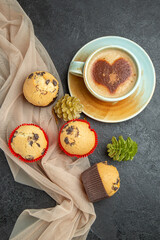Above view of delicious freshly baked small cupcakes and a cup of frothy coffee on towel accessory on black background