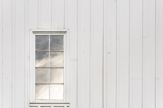 Closeup Of Exterior Of White Traditional Barn With Window Reflecting The Sky
