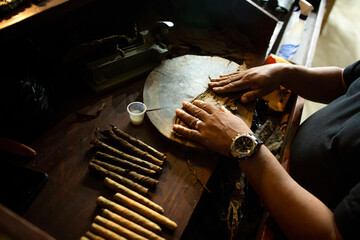Close-up of black man hands roll cigars from tobacco leaf at the cigar factory in Latin America. 