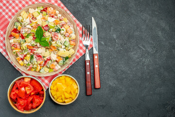 top view of bowl of vegetable salad on red napkin with veggies and cutleries on side and with free place for text on dark table